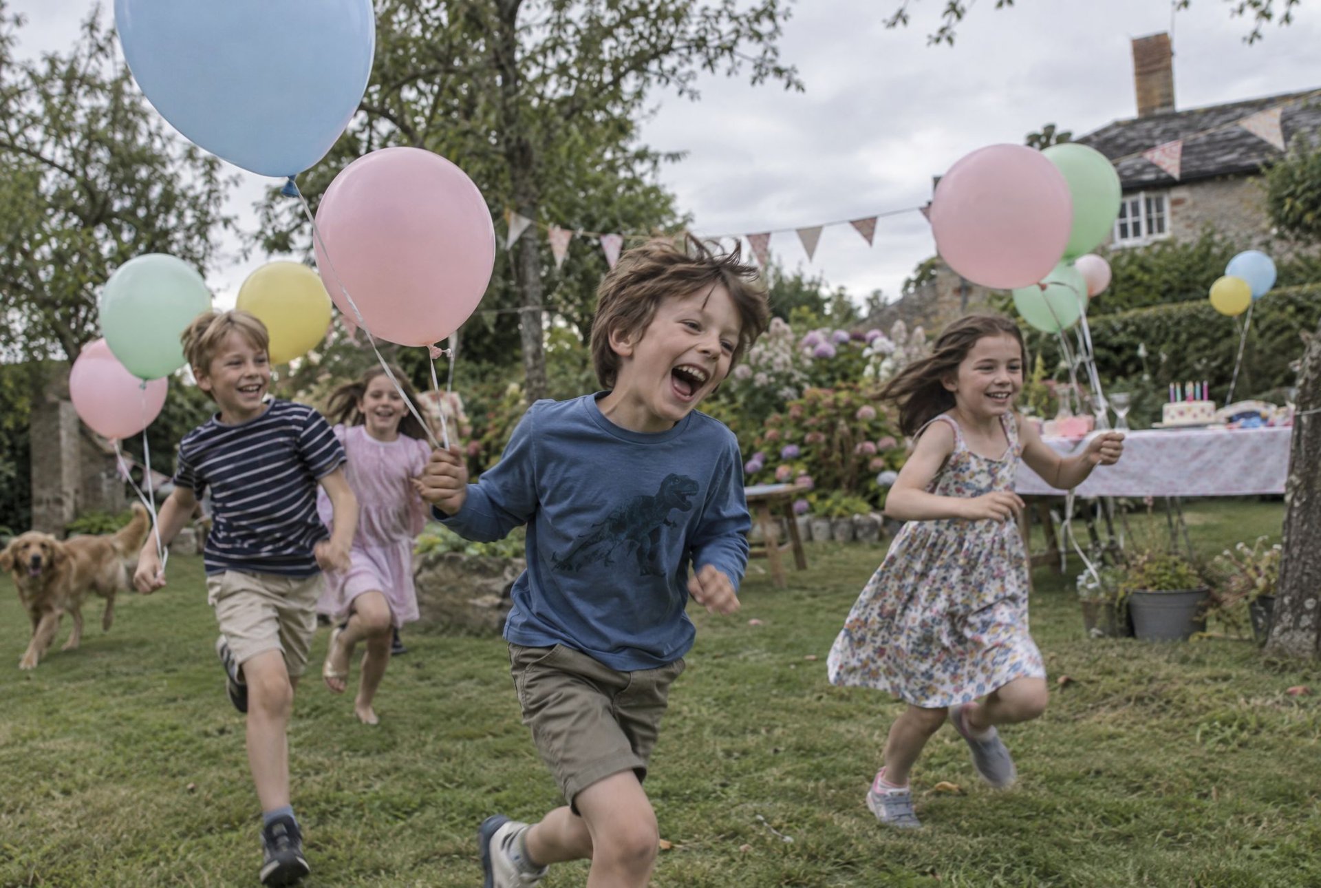 Enfants courant avec des ballons roses et blancs dans un jardin décoré pour un anniversaire