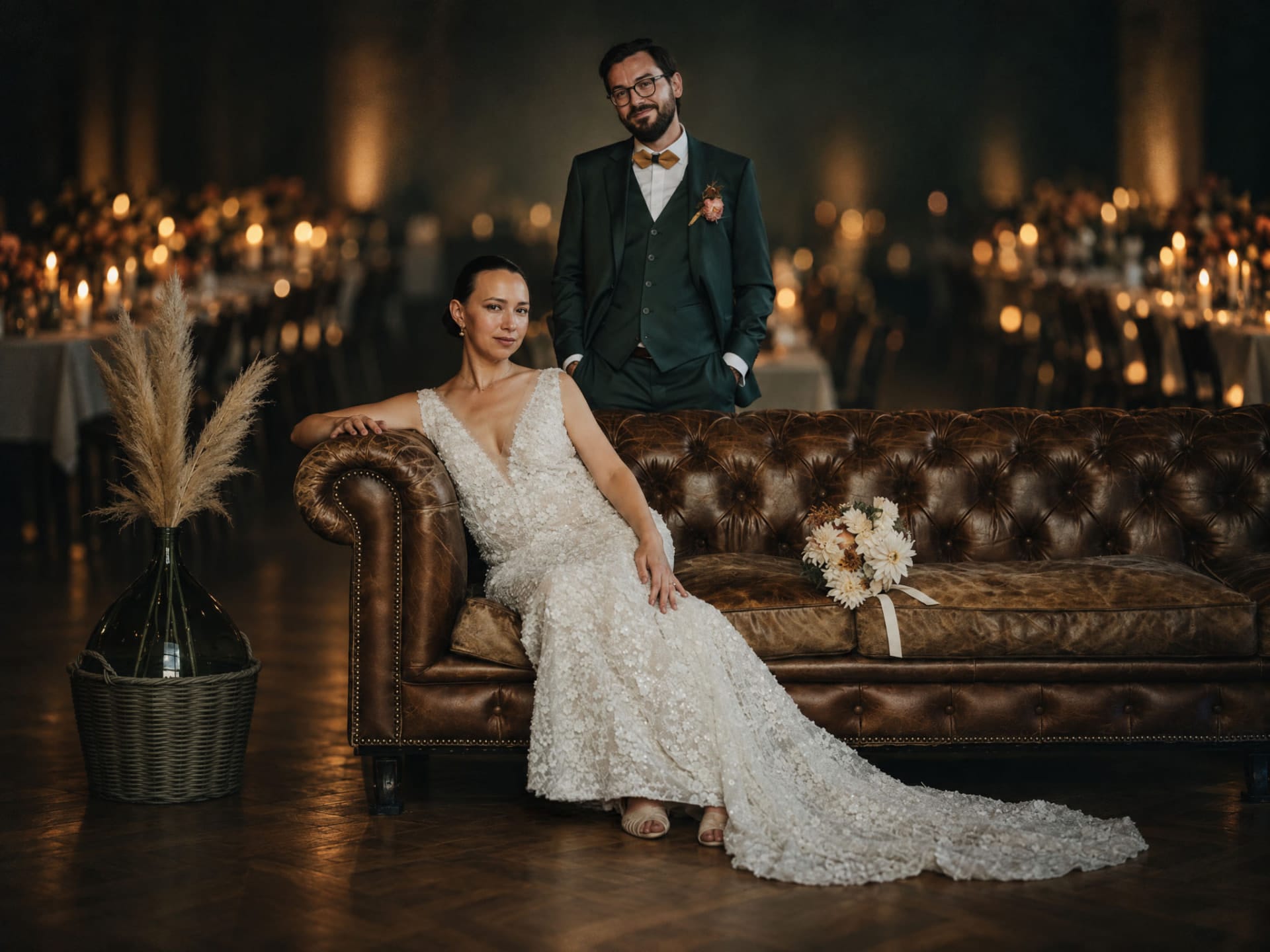 Bride and groom on a leather Chesterfield sofa in a candlelit reception room