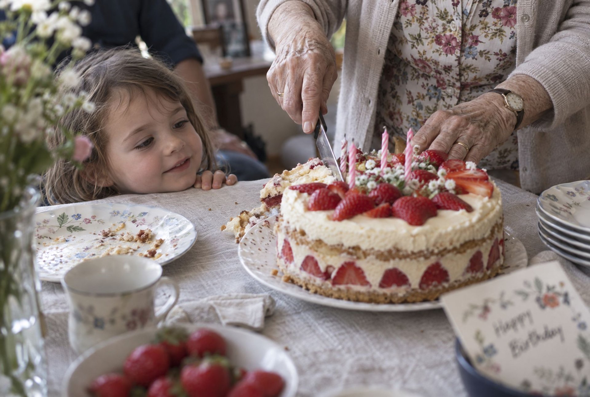 Enfant regardant une bougie allumée sur un gâteau d'anniversaire aux fraises préparé par sa grand-mère